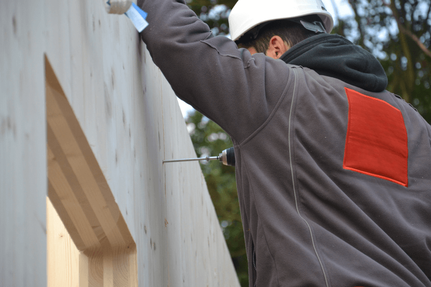 Photo représentant un charpentier qui installe un mur en bois de construction massif sur un chantier, pour illustrer le page Bois de construction – Hout Info Bois